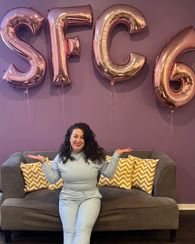 Reyna Hoerdeman Sitting On A Couch With Sfc 6 Balloons Celebrating Her 6Th Year In Business.
